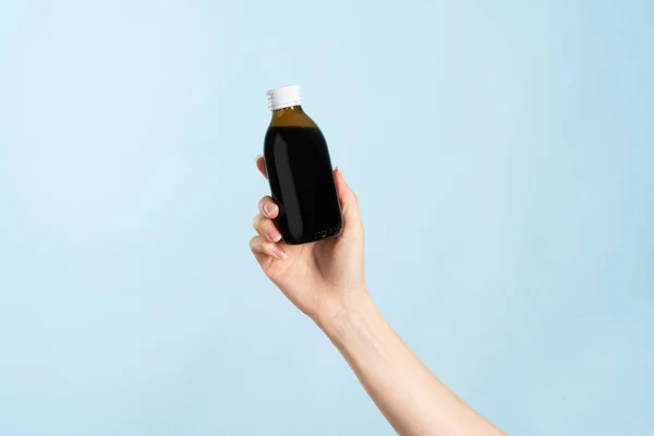 Image of hand holding a cold liquid medicine. Bottle without label for product placement. Everything on blue background