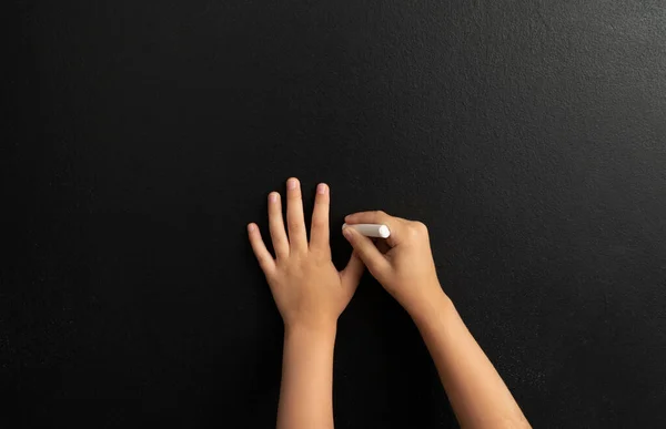 Image of little boy,s hands drawing picuters on the black chalk board.