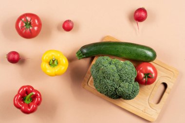 Açık bej arka planda çok taze sebzeler var. Mutfak malzemeleri, doğrama tahtası, bıçak, mutfak bezi ve örgü..