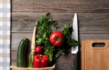 Fresh vegetables in the reusable shopping bag, picked straight from grocery farm shop lying lext to chopping board. Ready to make salad. Everything exposed on vintage wooden table