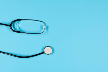Black stethoscope, top view on  the blue background. Medical equipment, tool for measuring the heart rate, lungs, and abdomen sounds
