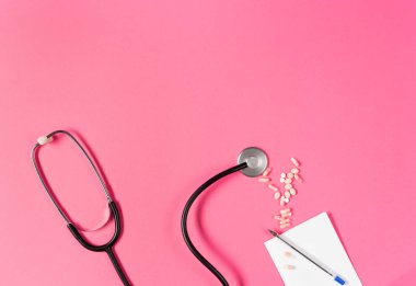 Top view of black stethoscope on the pink background.