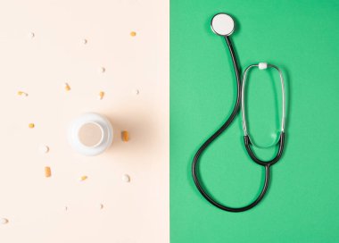 Top view of stethoscope, medication bottle and pills scattered all over the beige background. Medical equipment for measuring the heart rate, lungs, and abdomen sounds.