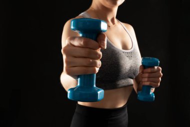 Close up photo of sporty girl working out with dumbbells on the black background