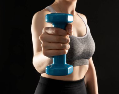 Close up photo of sporty woman working out with dumbbells on the black background