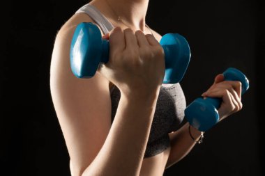 Close up photo of sporty woman working out with dumbbells on the black background