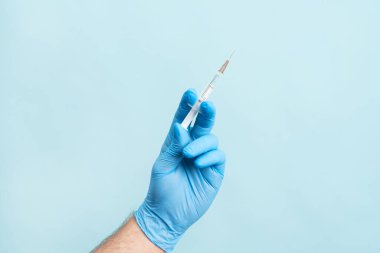 Close up picture of male hand with nitrile glove holding a syringe with vaccination on the blue background. Health care, vaccination cocncept.
