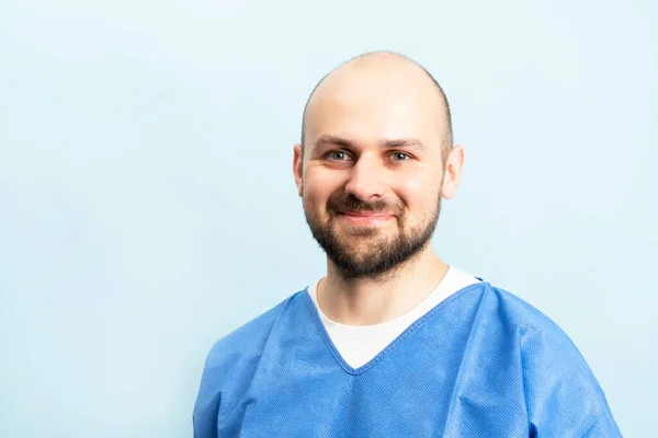 Portrait of smilin young and motivated doctor with stethoskope over neck and medical scrubs standing on the blue background.