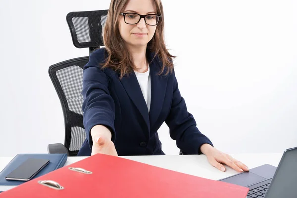 Young caucasian business woman reaches for binder with documents. Sitting by white desk in her work office