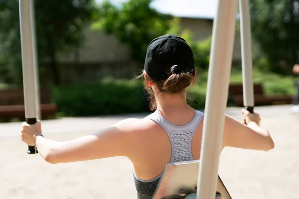 Youn athletic woman in active wear performing excersices on the machines in an outdoor park.