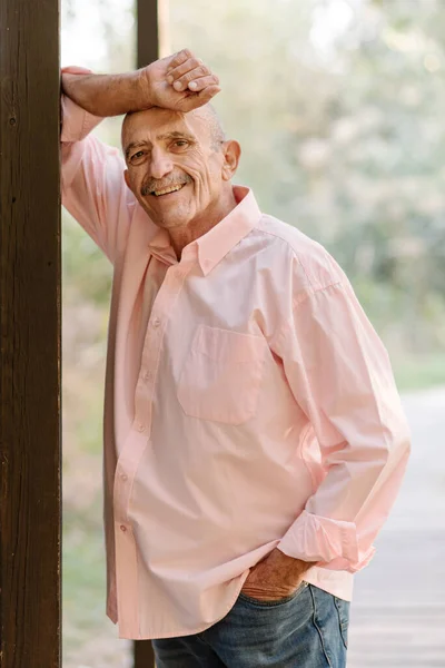 Sorridente uomo di mezza età in posa appoggiata a una colonna all'aperto. — Foto Stock