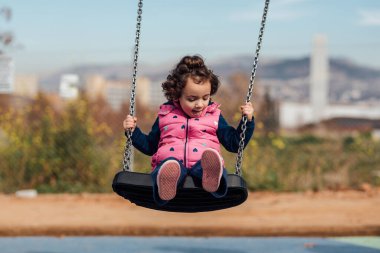 Küçük kız şehir parkında salıncakta sallanırken eğleniyor.