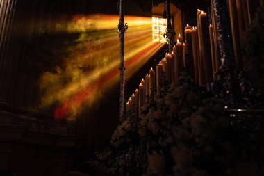 Procession during Holy Week in Sevilla, Andalucia, Spain. Incense smoke is seen in the beam of light coming in from the church window. 