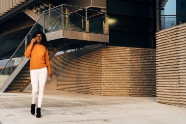 Sokakta yürürken telefonla konuşan genç Afro-Amerikalı kadın..