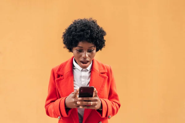 Mulher afro chocado olhando surpreendido em seu telefone móvel. — Fotografia de Stock