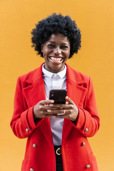 Afrikalı Amerikalı kadın kameraya bakıyor ve elinde cep telefonu tutarken gülüyor..