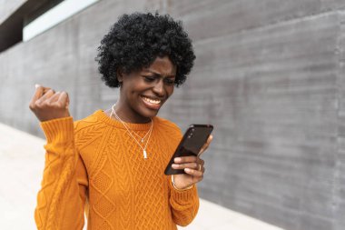 Afrikalı Amerikalı kadın cep telefonundan iyi haberler alırken kutlama yapıyor..