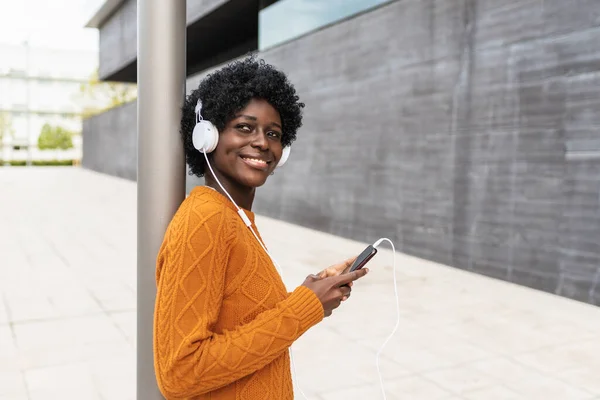 Siyahi bir kadın sokakta cep telefonu ve kulaklıkla müzik dinlemekten zevk alıyor..