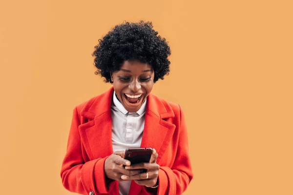 Šťastná černoška dívá vzrušeně na svůj mobilní telefon při použití venku. — Stock fotografie