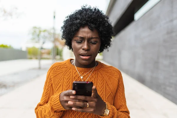 Afro mulher olhando surpreso com seu telefone celular ao receber notícias ou ler uma nova mensagem. — Fotografia de Stock