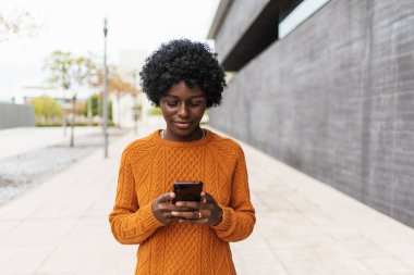 Sokakta yürürken akıllı telefon kullanan Afrikalı bir kadın..