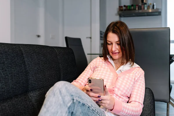 Mujer usando un teléfono móvil mientras está sentada en el sofá en casa. —  Fotos de Stock