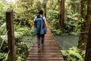 Ormanda yürüyüş yaparken asılmış bir köprüde yürüyen bir yürüyüşçünün arka görüntüsü.