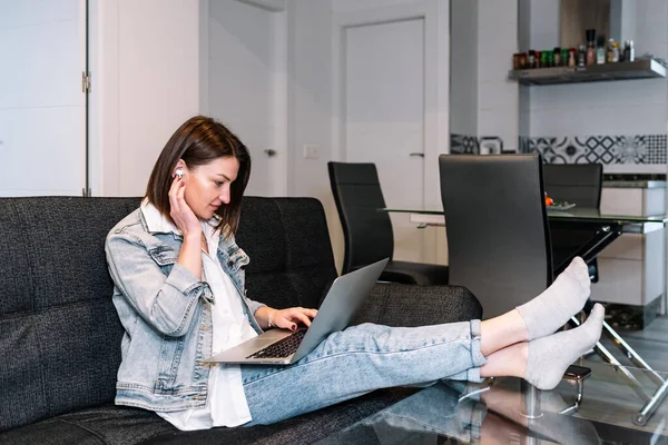 Mujer usando un portátil y auriculares inalámbricos mientras trabaja desde casa. —  Fotos de Stock