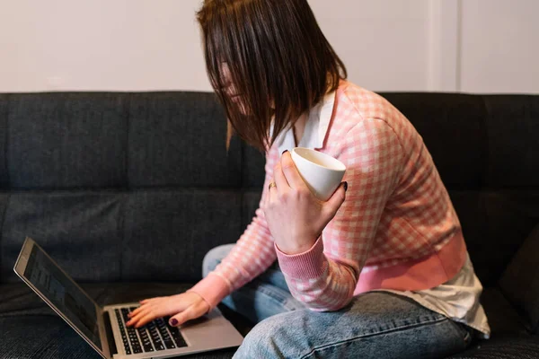 Mujer bebiendo una taza de café y usando un portátil mientras trabaja desde casa. —  Fotos de Stock
