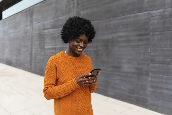 African woman smiling while using her smartphone in the street. — Stock Photo, Image