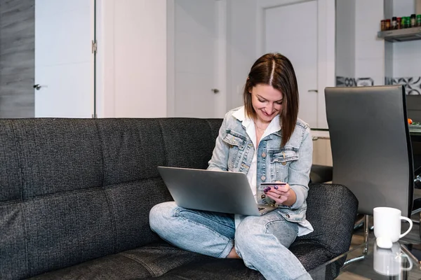 Mujer usando un portátil y una tarjeta de crédito mientras está sentado en el sofá en casa. —  Fotos de Stock