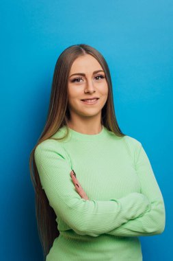 Kollarını kavuşturup izole bir arka planda gülümseyen genç bir kadın..