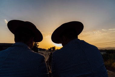 Tanınmayan adamlar gün batımında at arabasıyla kırsaldan geçiyorlar..