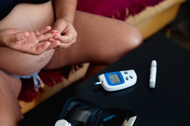 Pregnant woman checking sugar level with a glucometer device at home. Pregnancy and health concept.
