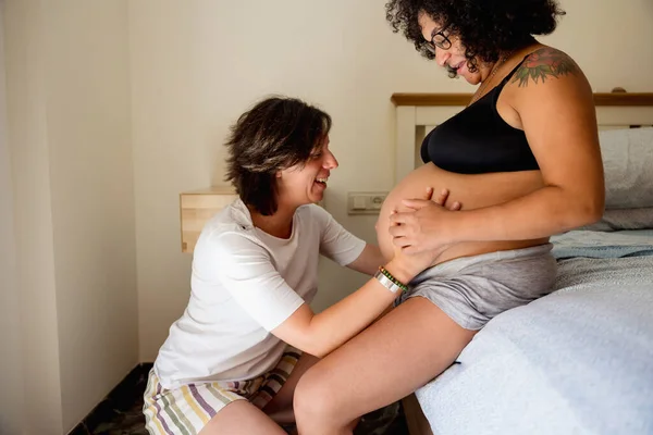Happy and excited woman touching the belly of her pregnant girlfriend. Pregnancy, lgbt and motherhood concept.