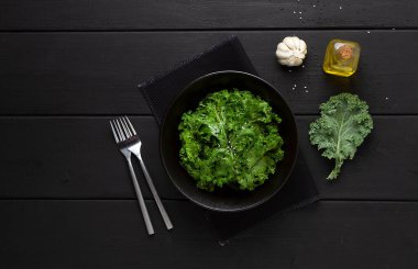 Kızarmış lahana yaprakları, baharatlar ve susam tohumlarıyla, siyah ahşap bir masanın üzerinde, üst manzara, yatay, insan yok.,