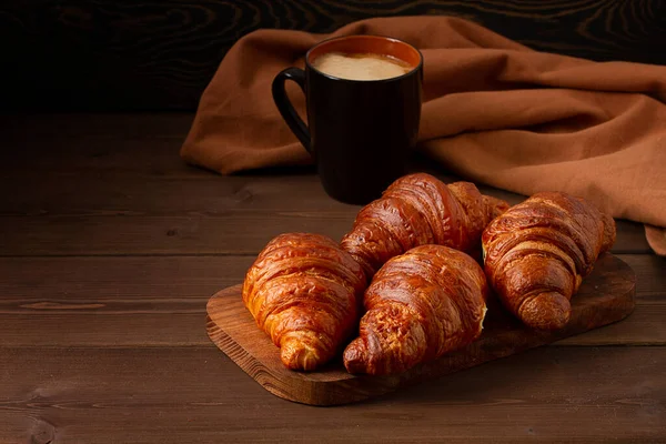 Pastéis, Croissants em uma mesa de madeira marrom, com uma xícara de café, café da manhã, sem pessoas, estilo rústico, — Fotografia de Stock