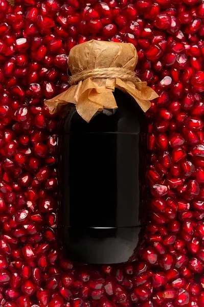 Pomegranate sauce in a bottle, top view, in pomegranate seeds, food background, vertical, no people,