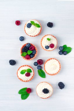 Krem şantili ve taze dutlu mini turtalar, beyaz bir masada, bulanık odaklı, yatay, insan yok.,