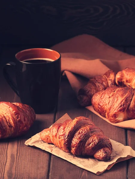 Pastéis, Croissants em uma mesa de madeira marrom, com uma xícara de café, café da manhã, sem pessoas, estilo rústico, — Fotografia de Stock