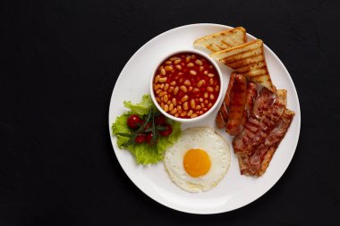 Geleneksel İngiliz kahvaltısı, siyah arka planda, kızarmış pastırmalı yumurta, sosis, beyaz fasulye, vişneli domates, yatay, insan yok. Yüksek kalite fotoğraf