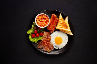 Geleneksel İngiliz kahvaltısı, siyah arka planda, kızarmış pastırmalı yumurta, sosis, beyaz fasulye, vişneli domates, yatay, insan yok. Yüksek kalite fotoğraf