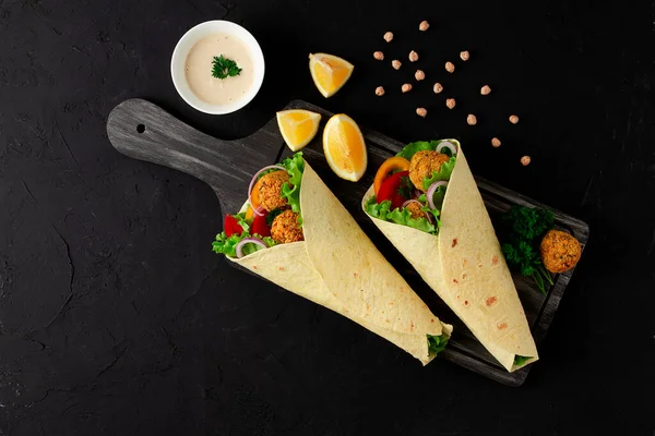 Tortillas avvolto con palline di falafel e verdure fresche, cibo sano vegetariano, su uno sfondo nero, nessuna gente, — Foto Stock