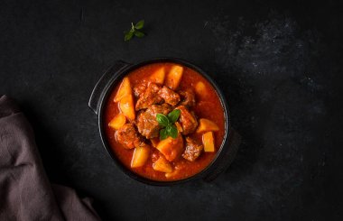 Patatesli, domates soslu, baharatlı ve otlu, yakın plan, insan yok, siyah arka planda.