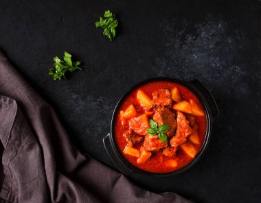 Patatesli, domates soslu, baharatlı ve otlu, yakın plan, insan yok, siyah arka planda.