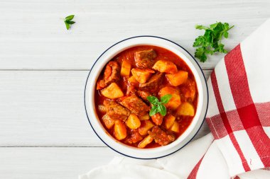 Etli, domates soslu, baharatlı ve otsuz patatesler beyaz bir masada.,