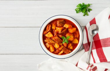 Etli, domates soslu, baharatlı ve otsuz patatesler beyaz bir masada.,