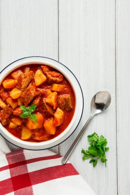 Etli, domates soslu, baharatlı ve otsuz patatesler beyaz bir masada.,