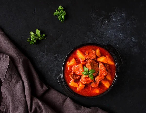 Patatesli, domates soslu, baharatlı ve otlu, yakın plan, insan yok, siyah arka planda.