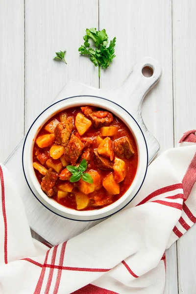 Etli, domates soslu, baharatlı ve otsuz patatesler beyaz bir masada.,